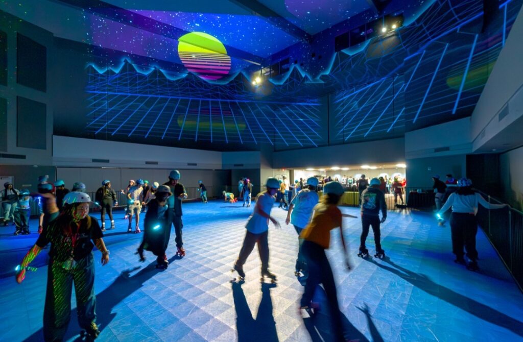 Matadors skate through the roller rink at Matador Nights while '80s retro-themed graphics are projected behind them.