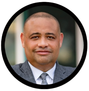 Dr. Joshua Fredeburg smiling looking straight at the camera. He is wearing a gray suit and gray tie with a white collared shirt.