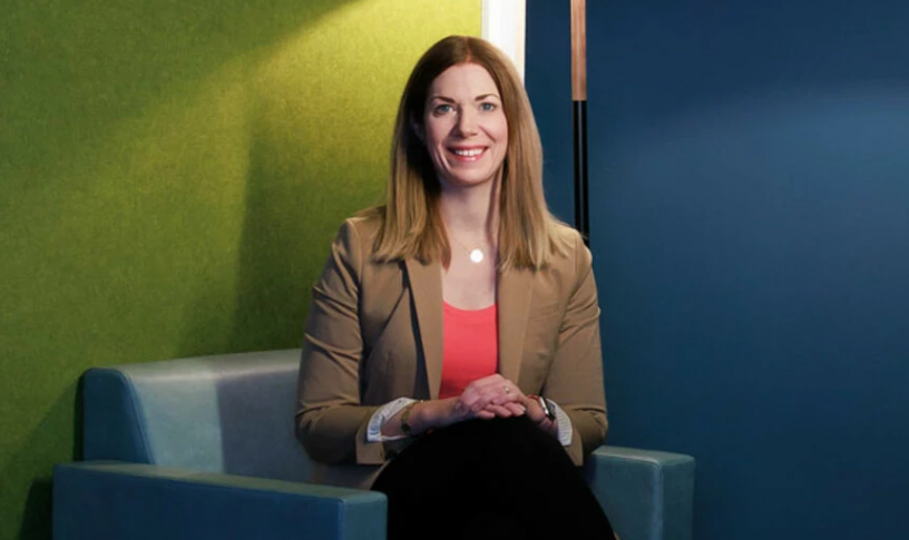 A woman, professionally dressed, sitting on a couch.