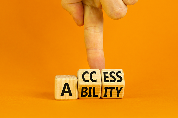Wooden blocks spelling "ACCESSIBILITY" on an orange background with a hand touching the blocks.