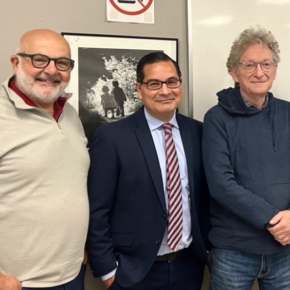 Three men, all wearing glasses, pose for a photo