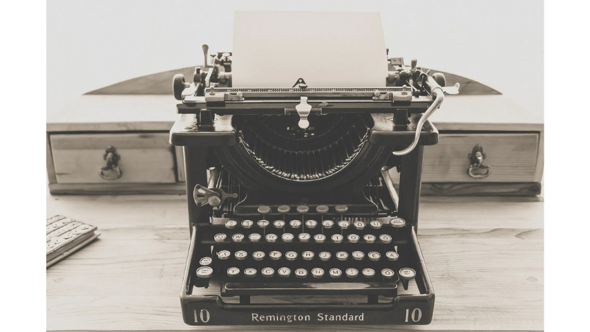 A Remington Standard typewriter holding a black sheet of paper, atop a desk