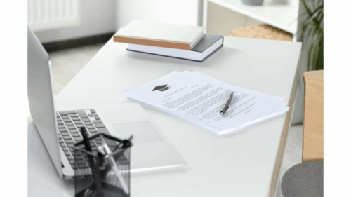 Workspace with a laptop, documents, books, and a pen on a white desk.