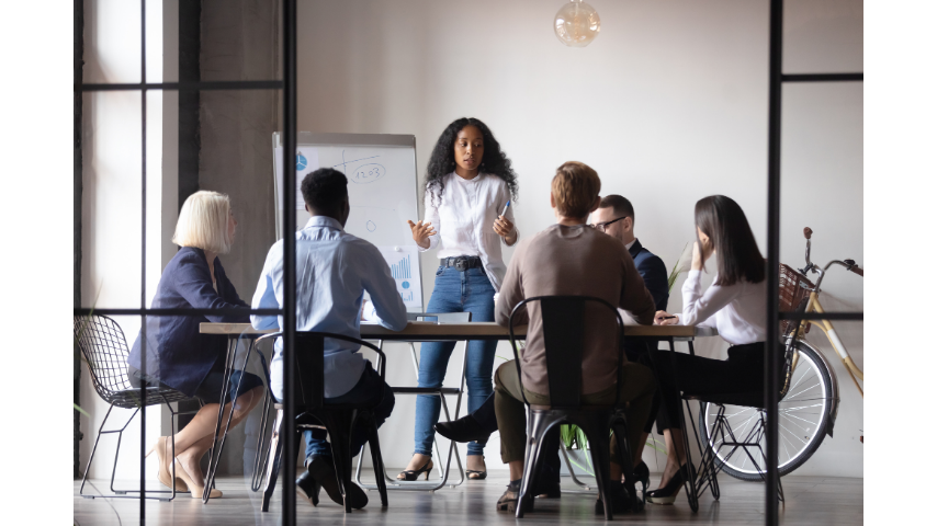 A woman presenting to colleagues around a table in a modern office setting.