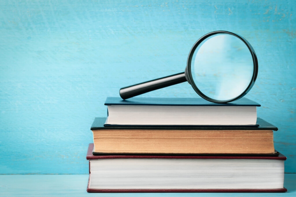 A magnifying glass on a stack of books on a blue wooden bookshelf with space for text.