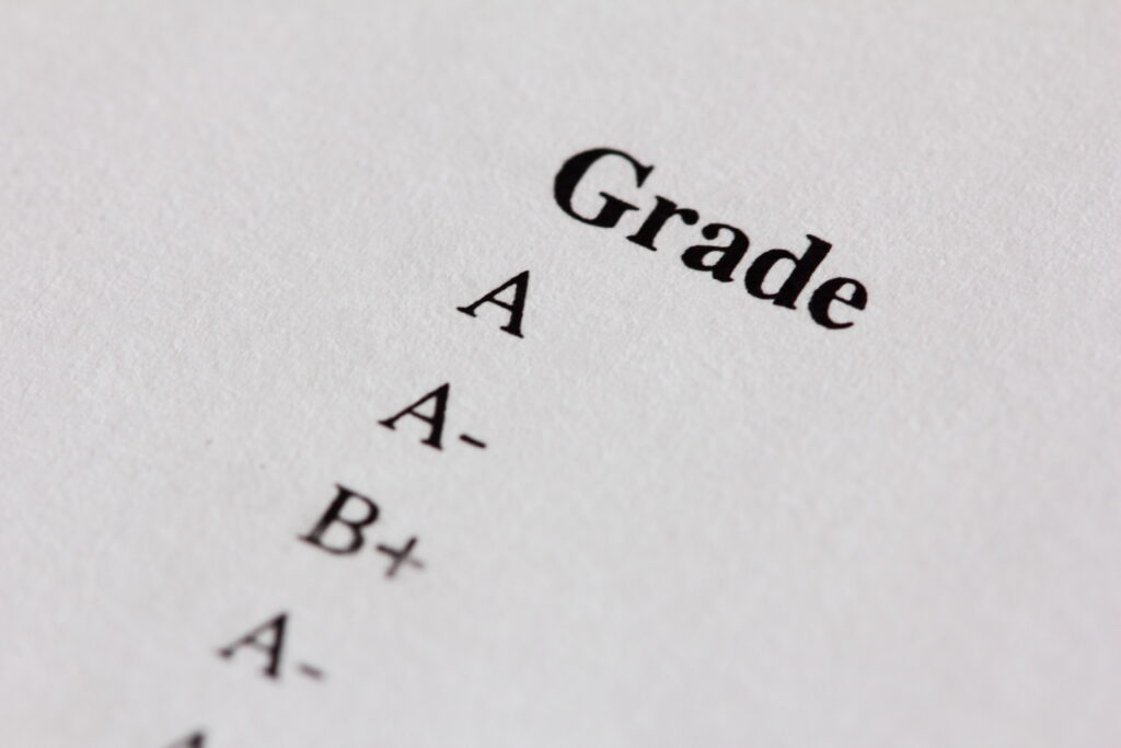 Close-up of a list of grades on a white paper, including A, A-, and B+.