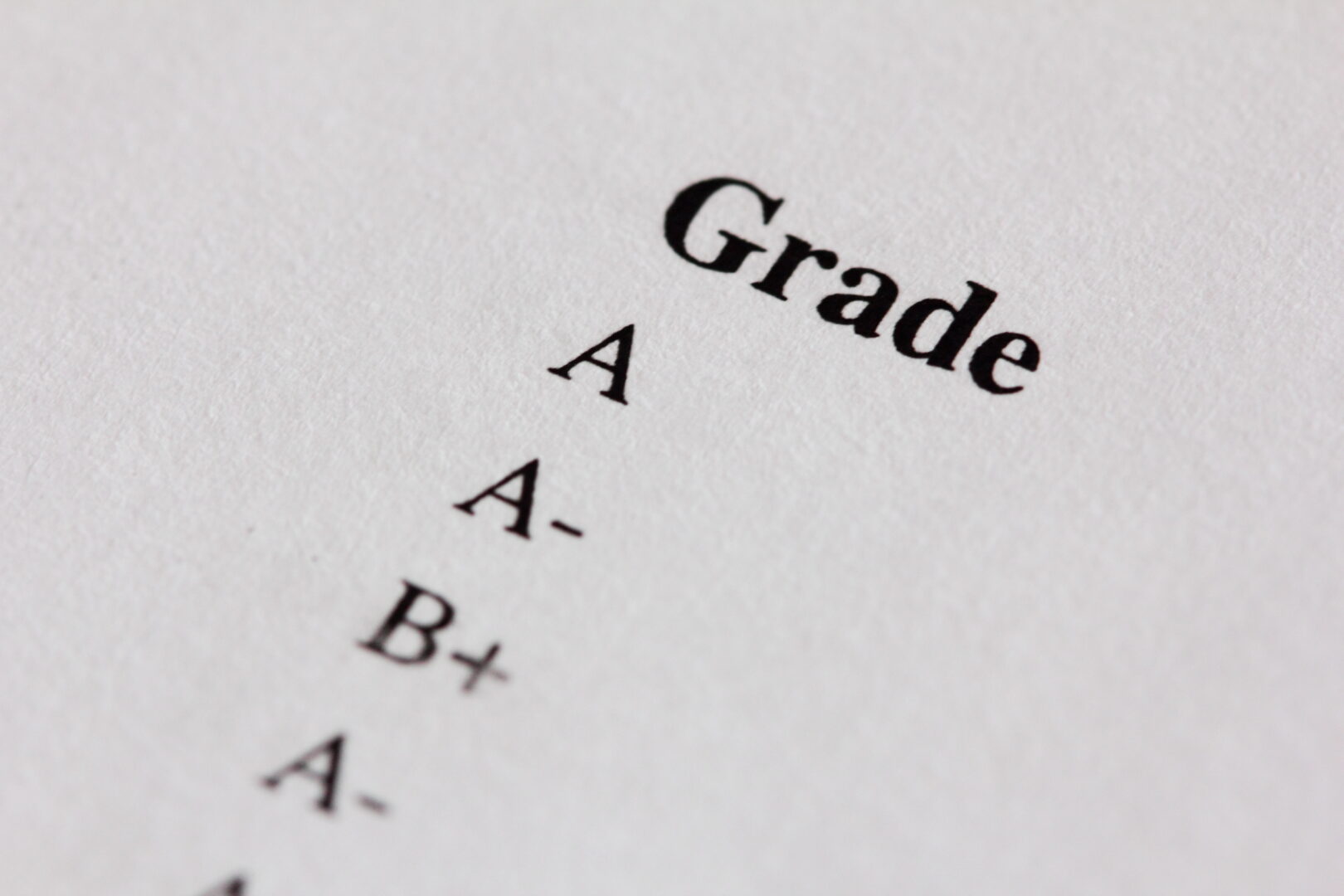 Close-up of a list of grades on a white paper, including A, A-, and B+.