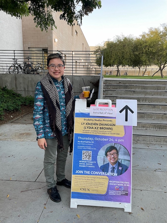 Ly XZ Brown stands by the poster for their event