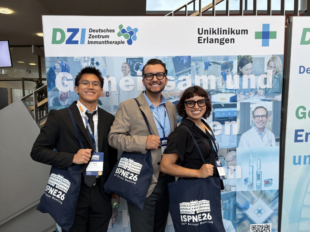 3 students happily pose with tote bags in front of a banner for the Public Health Conference in Germany.