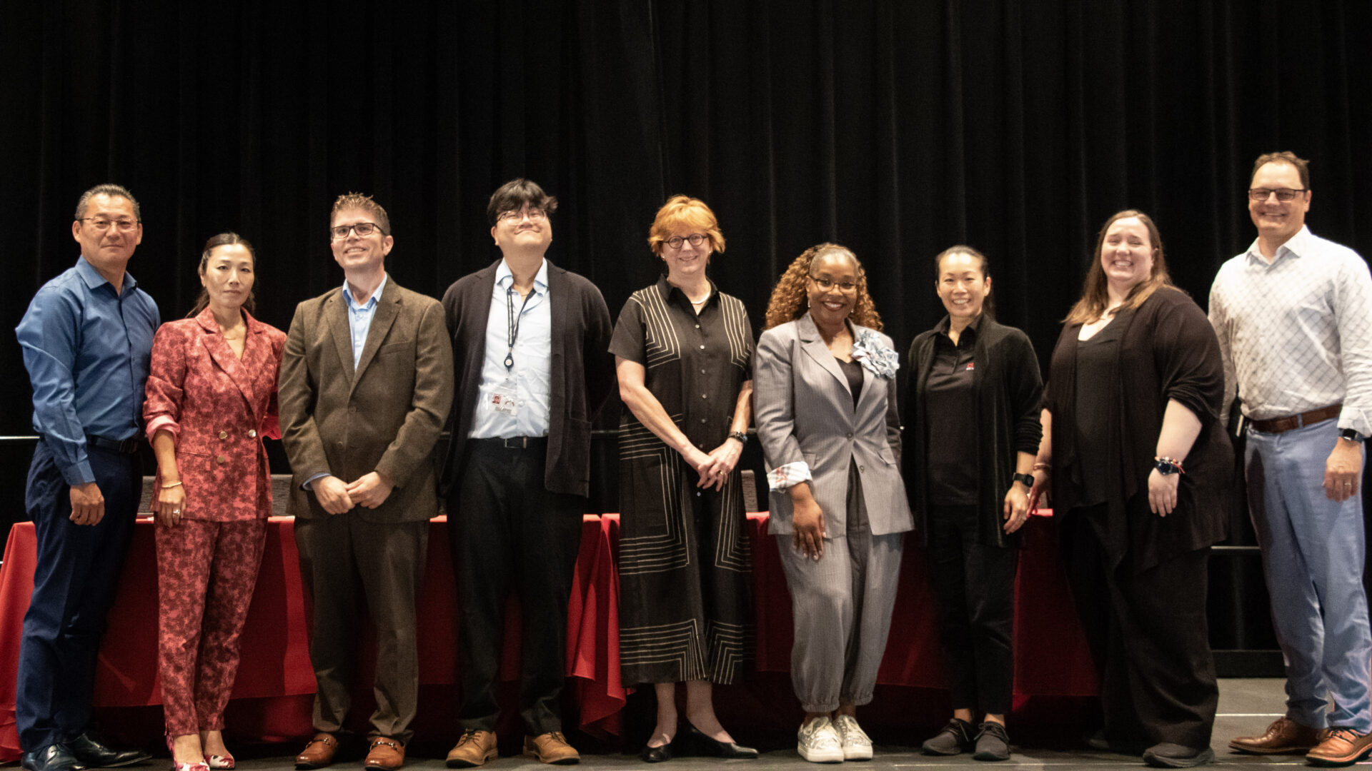 Nine participants at the R.I.S.E. Gerontology and Health Careers Conference pose together on a stage in front of black curtains